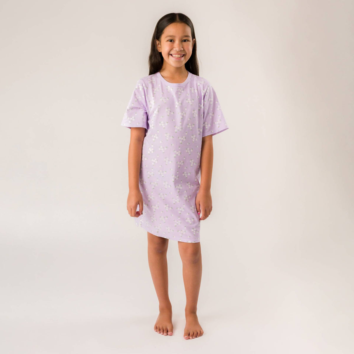 A young girl wearing a lilac purple summer nightie with an all over floral print. 