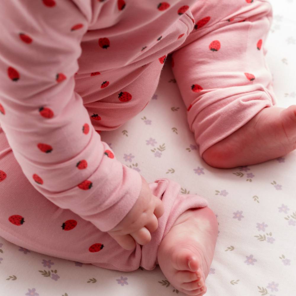 Baby in pink pajamas with strawberry pattern on a floral blanket