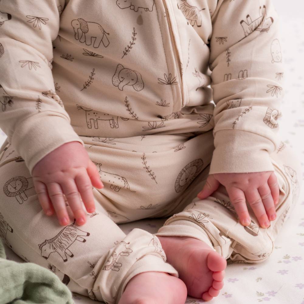 Baby in cream-colored outfit with animal prints sitting on a soft surface.