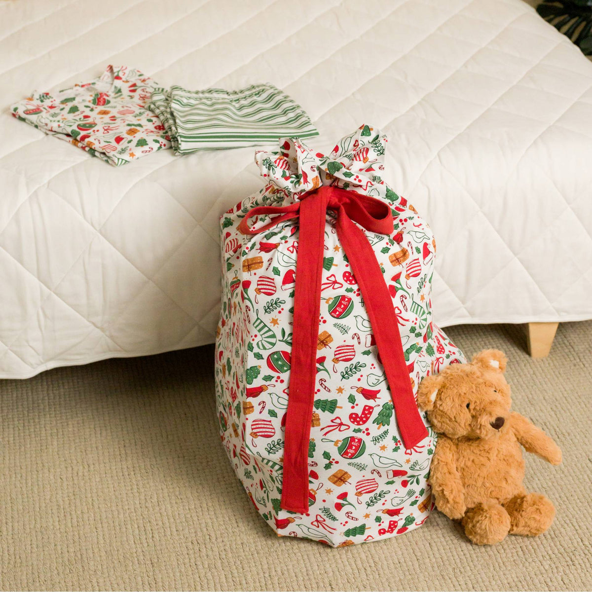 A filled Santa sack sitting next to a teddy bear. 