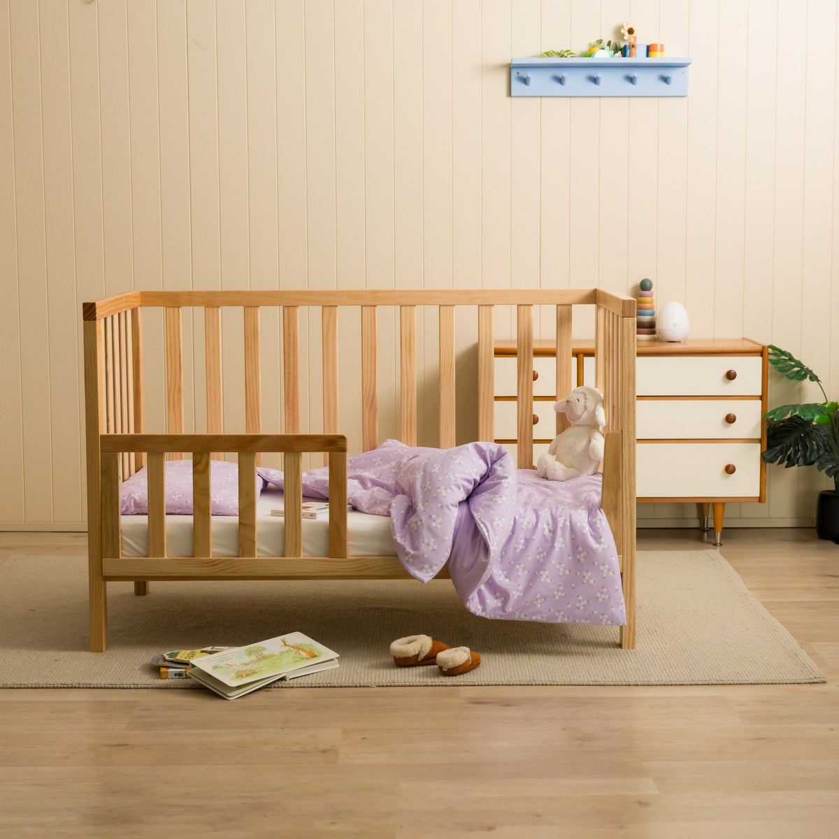 Nursery setting with a cot featuring a lilac daisy duvet cover. 