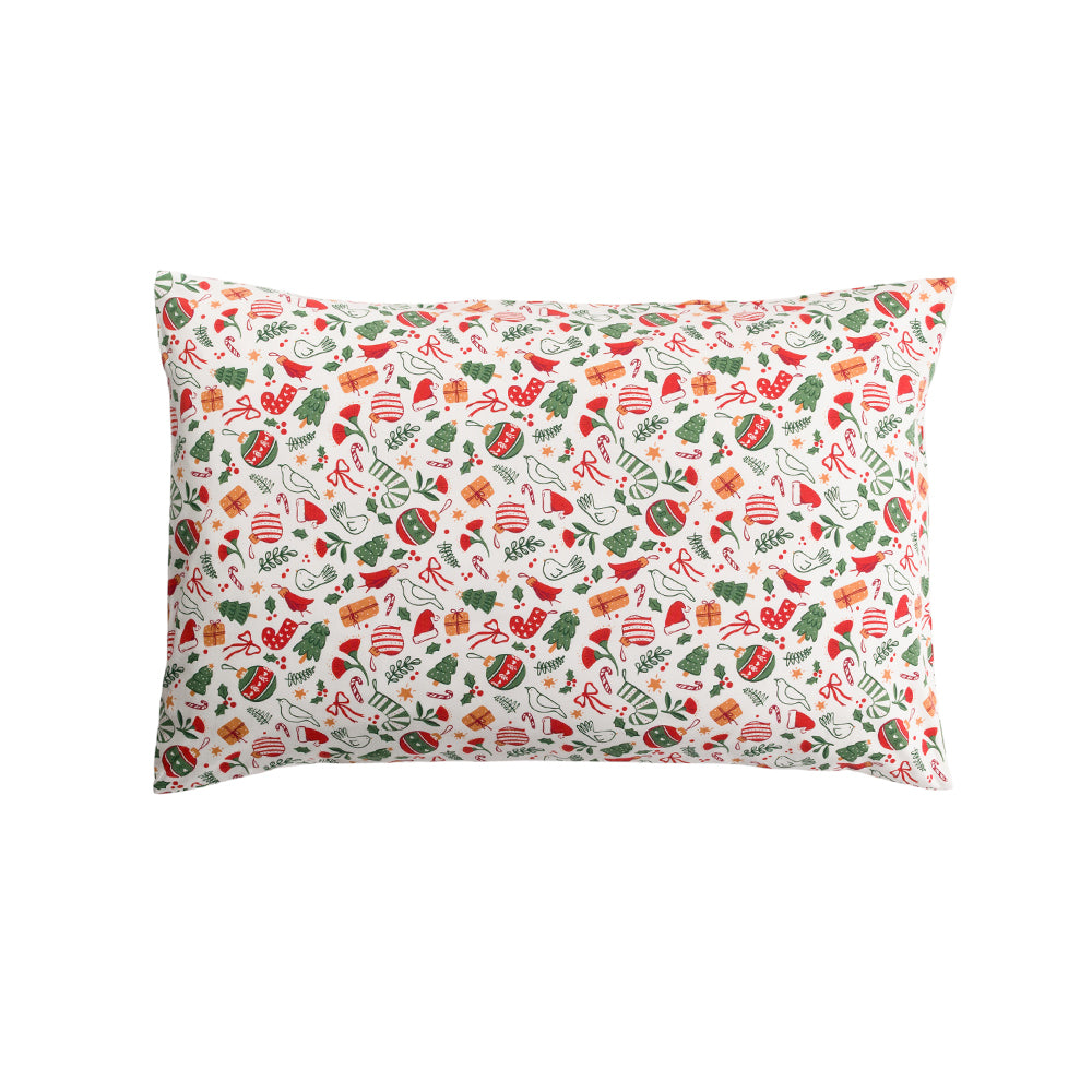 A rectangular throw pillow featuring a festive Christmas-themed pattern with red ornaments, green holly, candy canes, pine trees, and gift boxes on an off-white background.