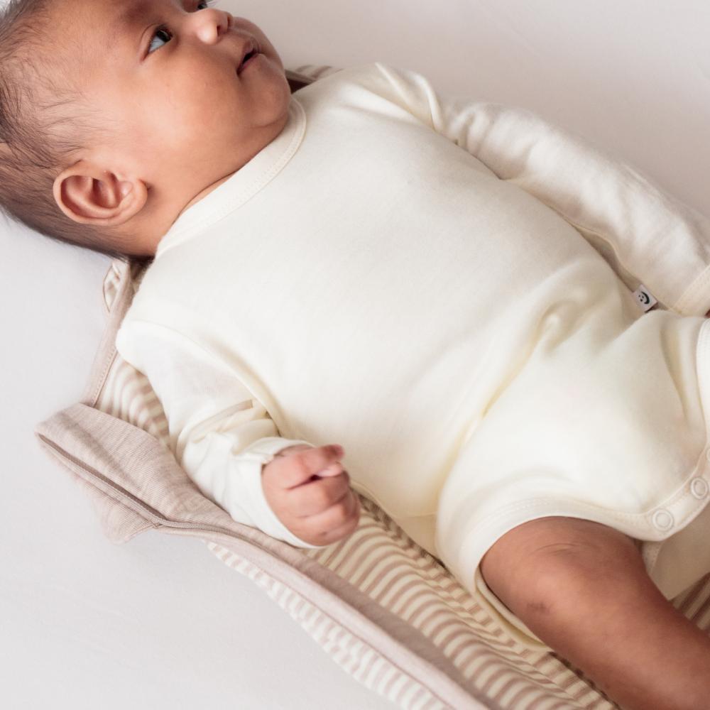 Baby wearing a white onesie lying on a textured surface