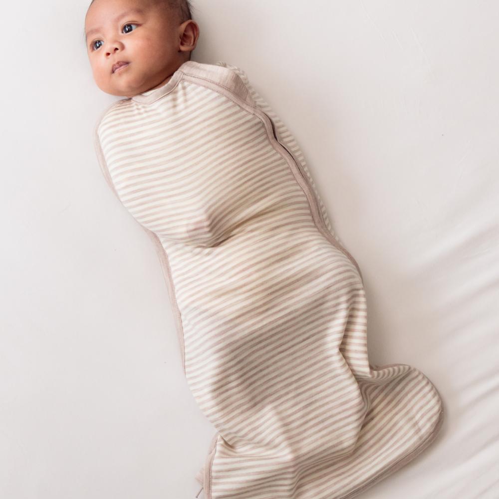 Baby swaddled in a beige swaddle on a white background