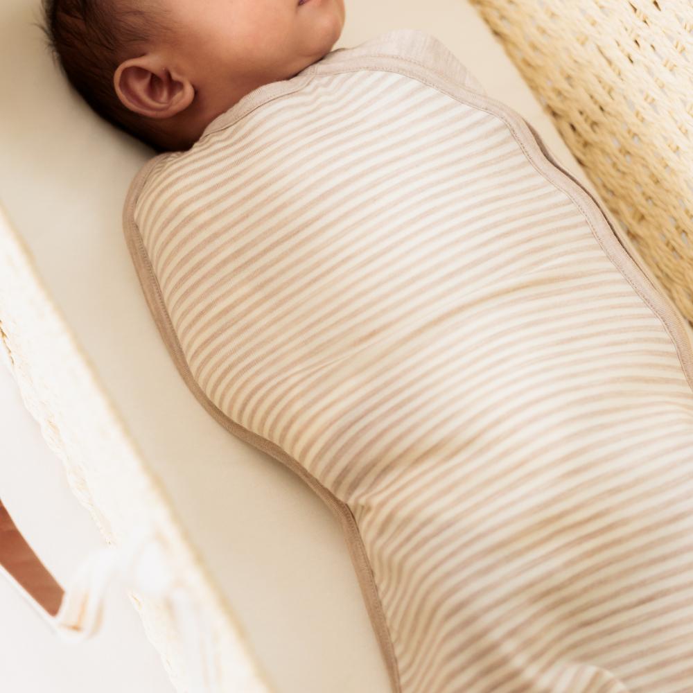 Newborn baby swaddled in a beige textured blanket on a white surface.