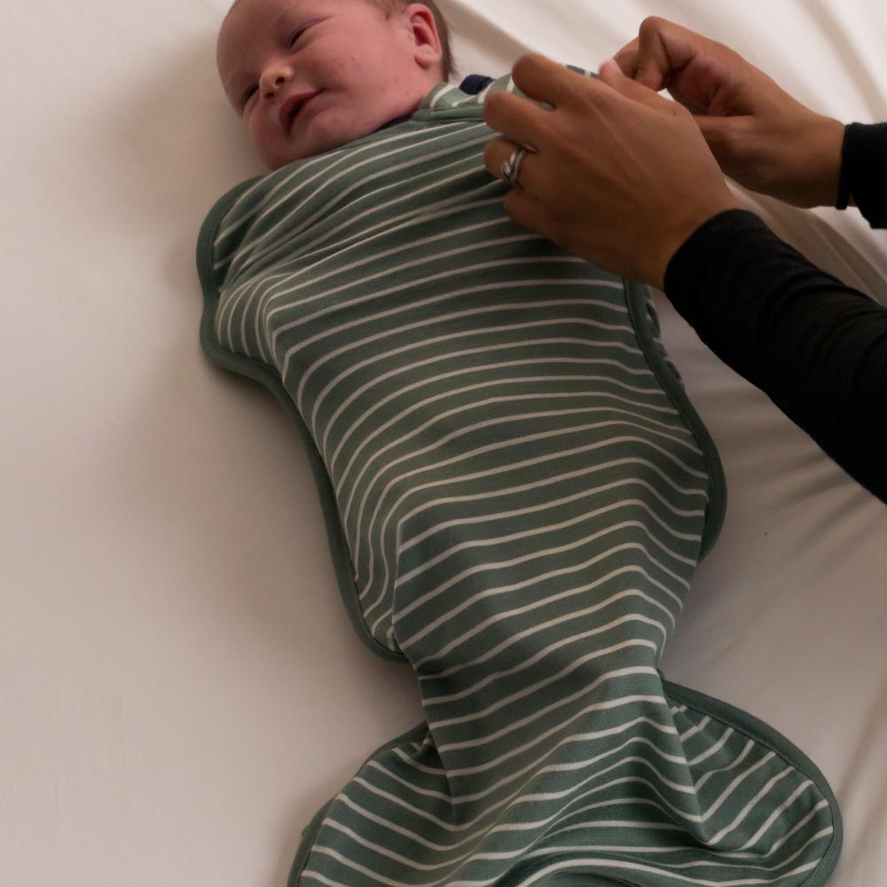 Baby wrapped in a green and white striped swaddle on a white surface