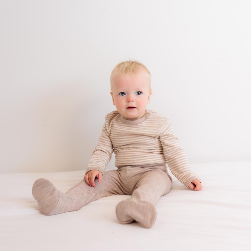 Baby sitting on a white surface wearing a beige striped merino outfit.