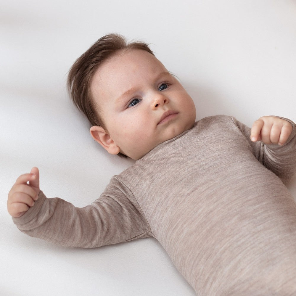 Baby wearing a brown onesie lying on a white surface