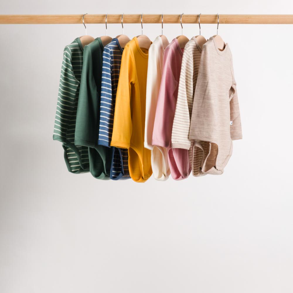 Colorful baby bodysuits on a wooden rack against a white background