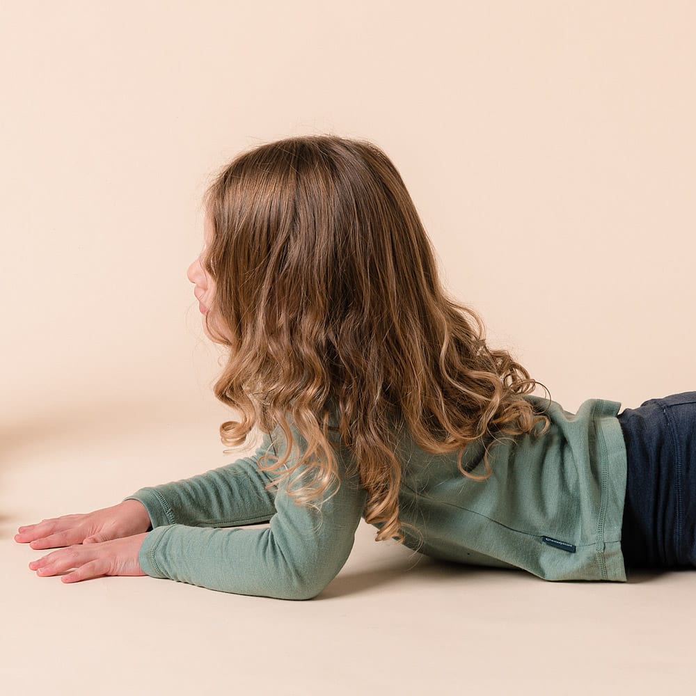 Person wearing a green merino long sleeve shirt on a beige background