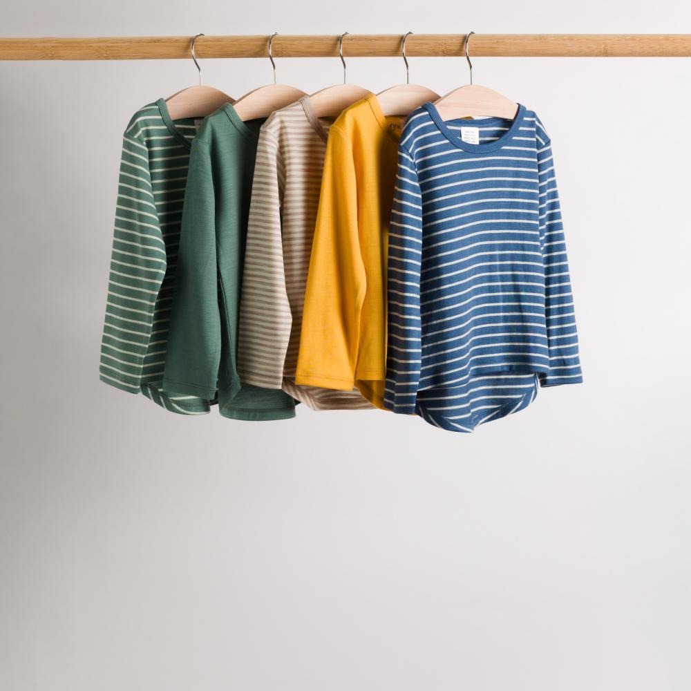Four children's merino long sleeve shirts in green, beige, yellow and blue hanging on a pole