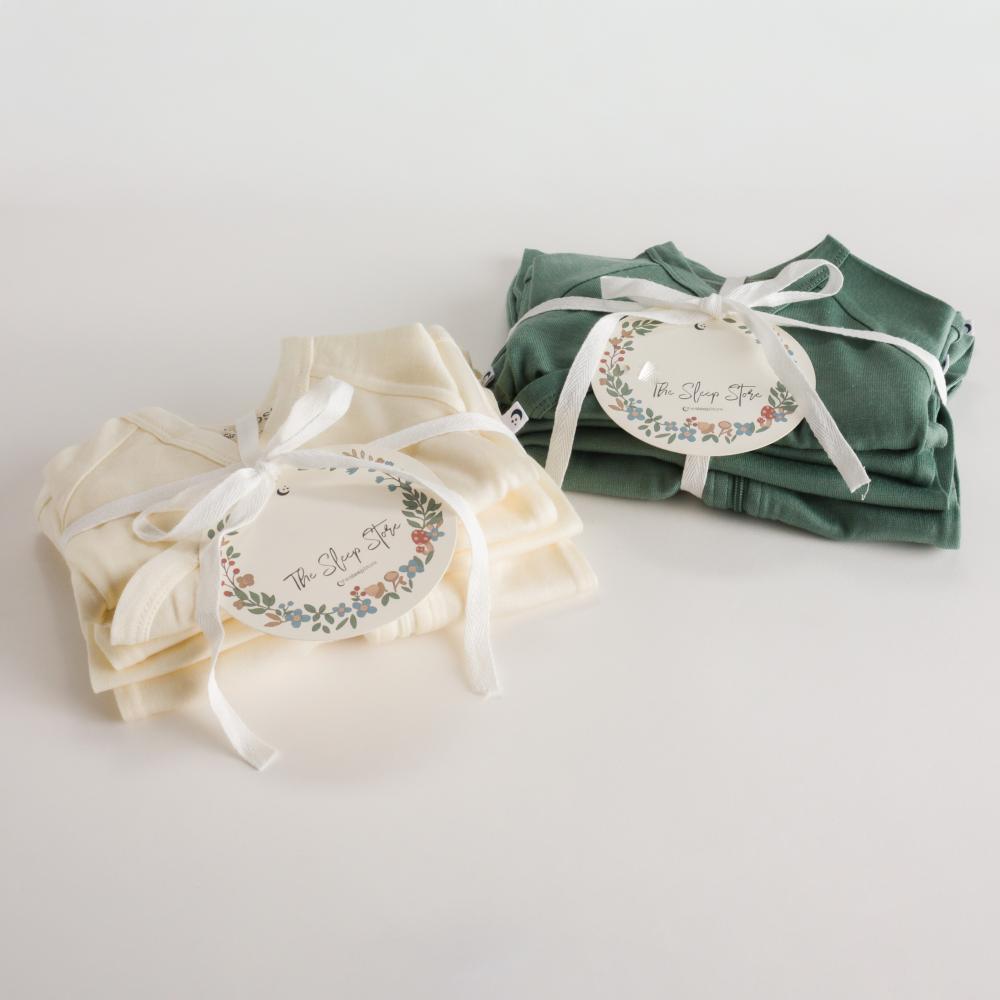 Two folded jersey merino clothing packs, one cream and one green, tied with ribbons and tags on a light background