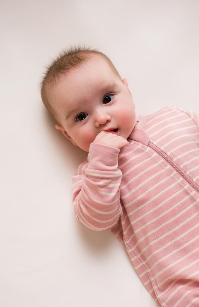 Baby in a pink striped merino onesie lying on a white surface