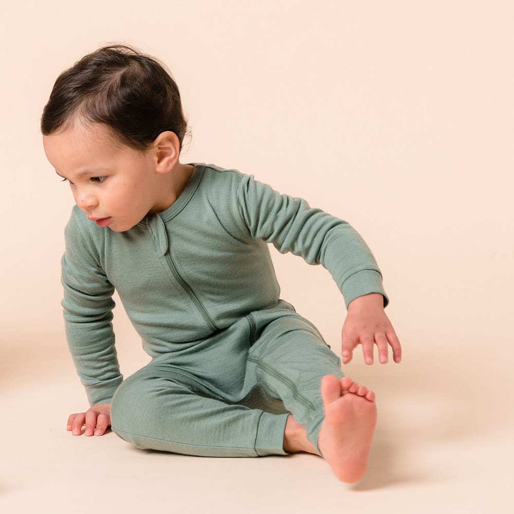 Child wearing a green merino onesie sitting on a beige background