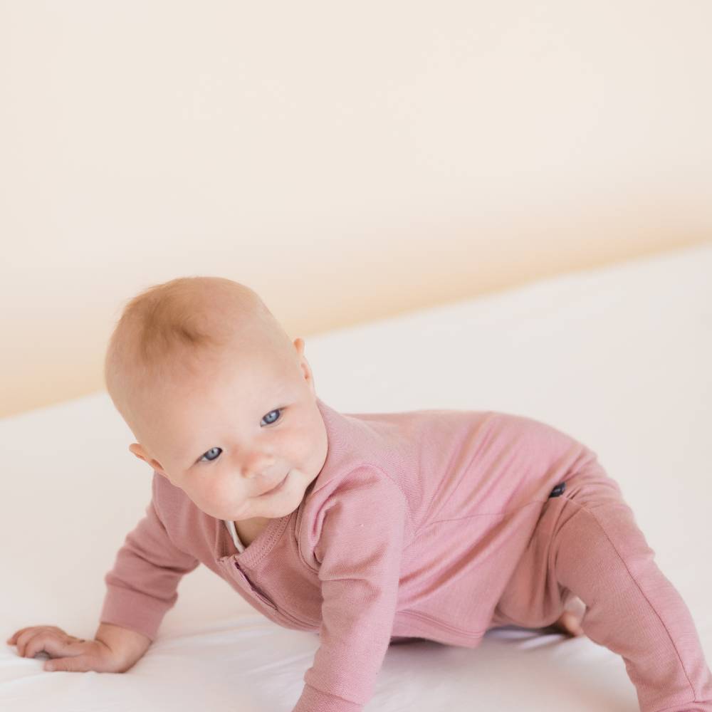 Baby in pink merino zip suit on a white surface with a light background