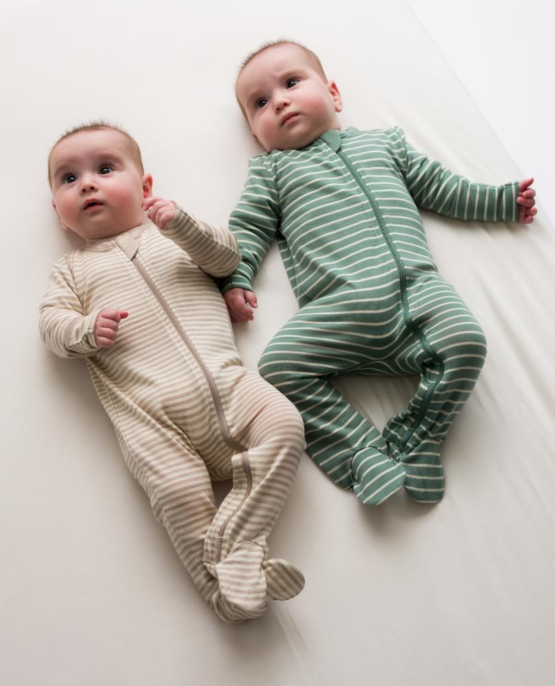 Two babies wearing merino striped onesies on a white surface