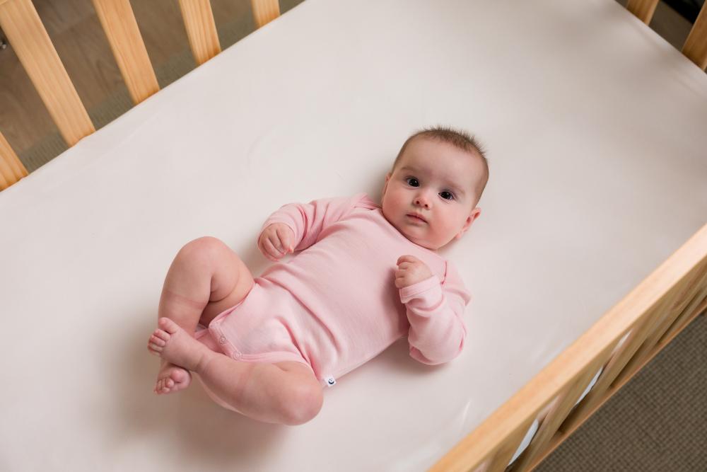 Baby in a soft pink deluxe merino bodysuit lying on a white mattress in a crib.