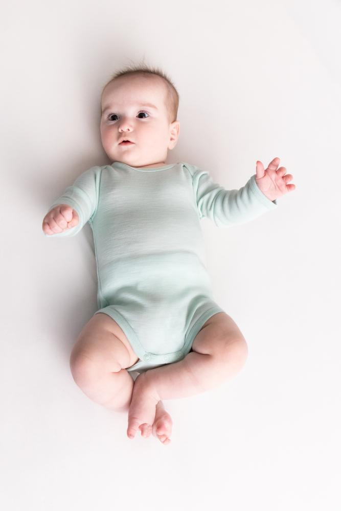 Baby wearing a light blue merino long sleeve bodysuit on a white background