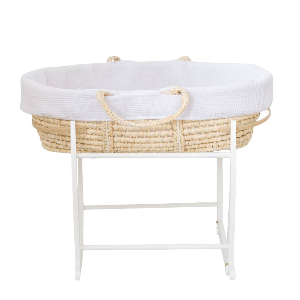 A Moses basket with a white textured fabric liner and rope handles, resting on a white wooden stand  shown against a plain white background.