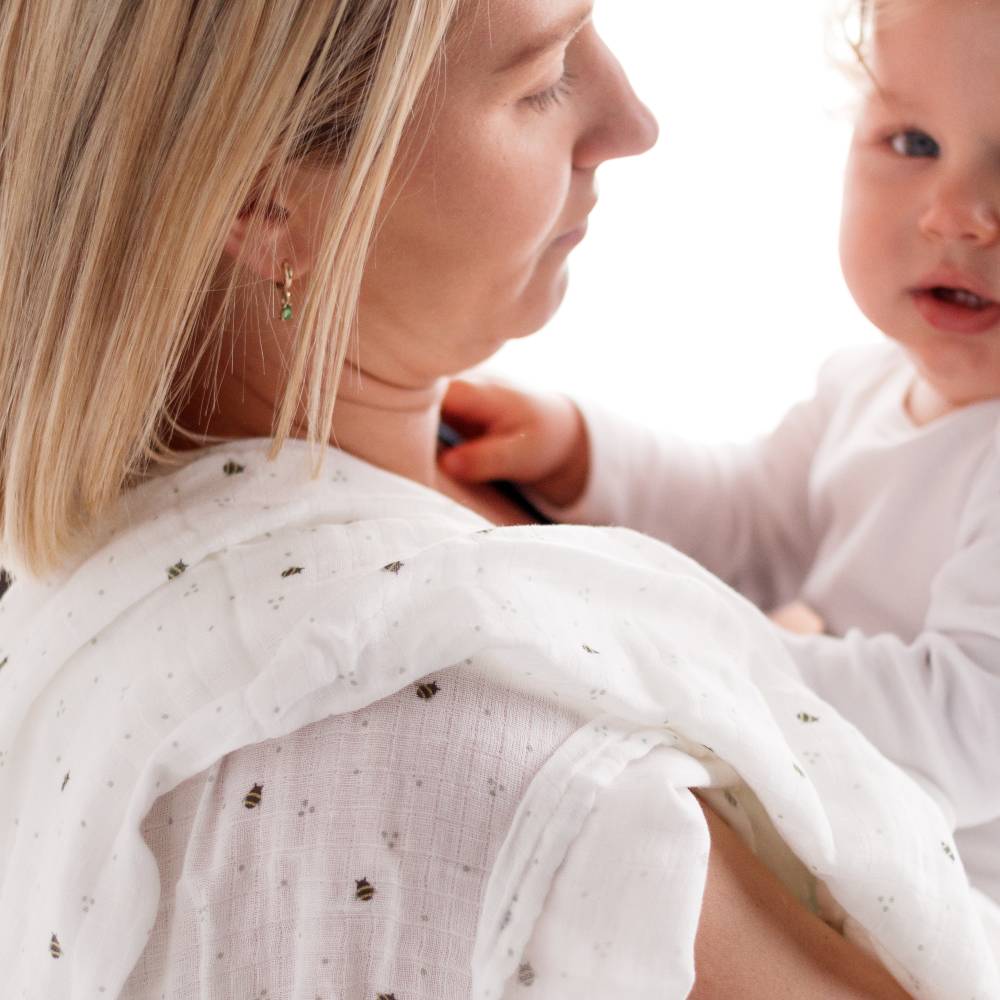 Woman holding baby with muslin wrap over her shoulder white with bee print