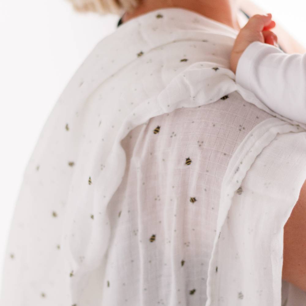 Woman holding baby with muslin wrap over her shoulder white with bee print