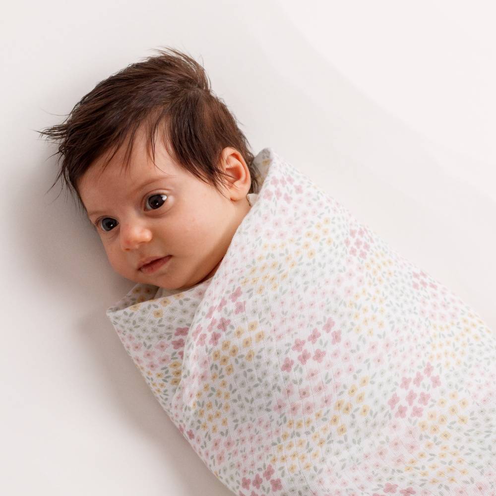 Baby wrapped in a floral muslin cotton blanket on a white background