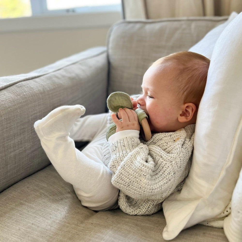 Baby lying on a couch holding a muslin cotton teething ring
