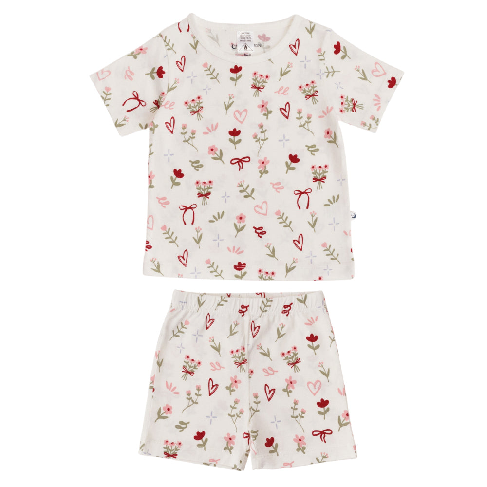 Kids short sleeve cotton pjs with an all over bows, flowers and hearts print on a white background. 