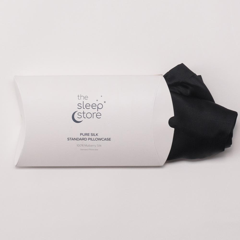 A folded black pillowcase partially pulled from a white cylindrical cardboard packaging sleeve, with the printed brand name 'the sleep store' visible on the sleeve, against a clean white background.