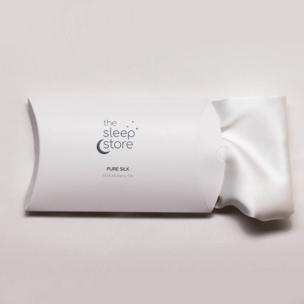 A white pillow-shaped cardboard package from The Sleep Store containing a Pure Silk pillow, with the white silk pillow partially pulled out from the right side, set against a light gray background.