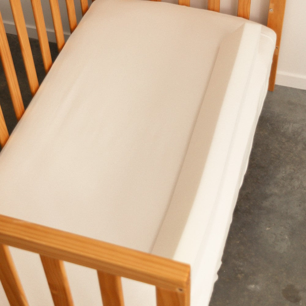 Wooden crib with a white mattress and bed bumper on the edge.