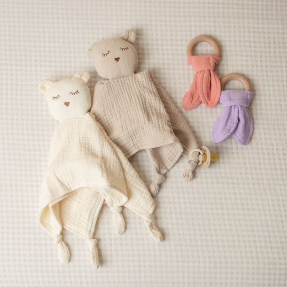 Baby comfort items including a plush toy, blanket, and teething rings on a textured surface.