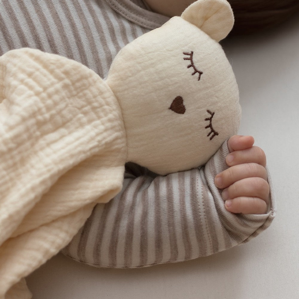 Close up of child holding a vanilla  plush bear toy wearing a brown striped long sleeve merino