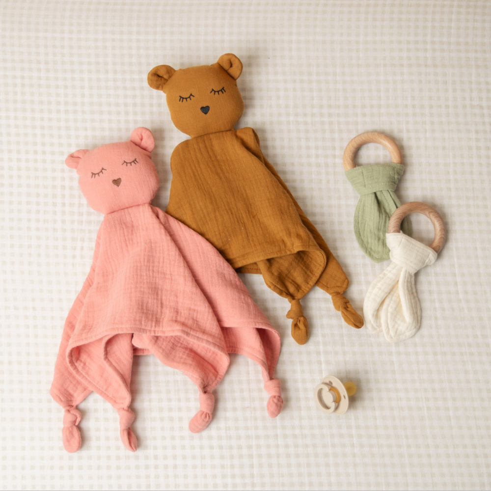 Two soft toys, one pink and one brown, and two teething rings on a textured surface.