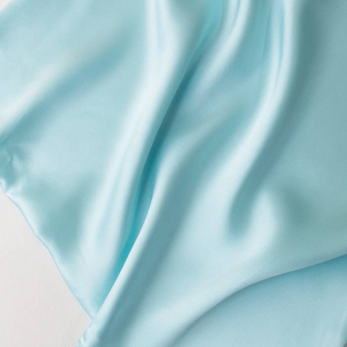 Close-up of light blue silk fabric with soft folds on a white background