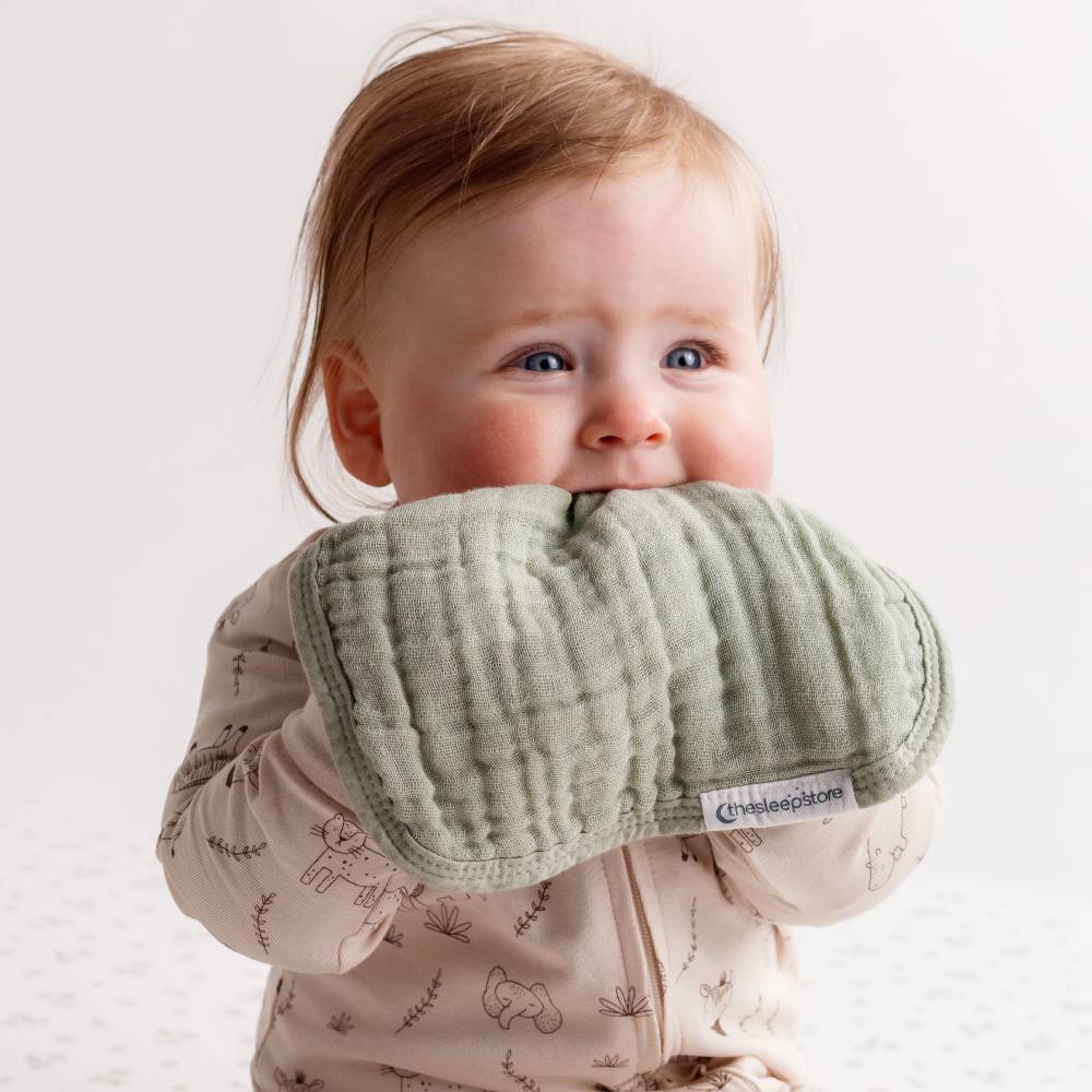 Baby holding a green face cloth with a visible brand label on a light background