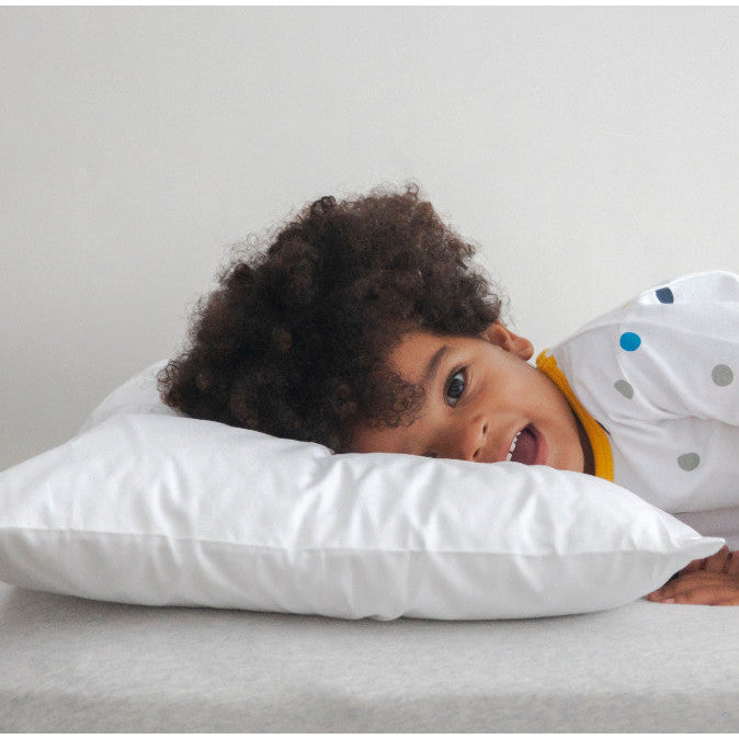 Child lying on a bed with a white pillow, wearing a polka dot outfit.