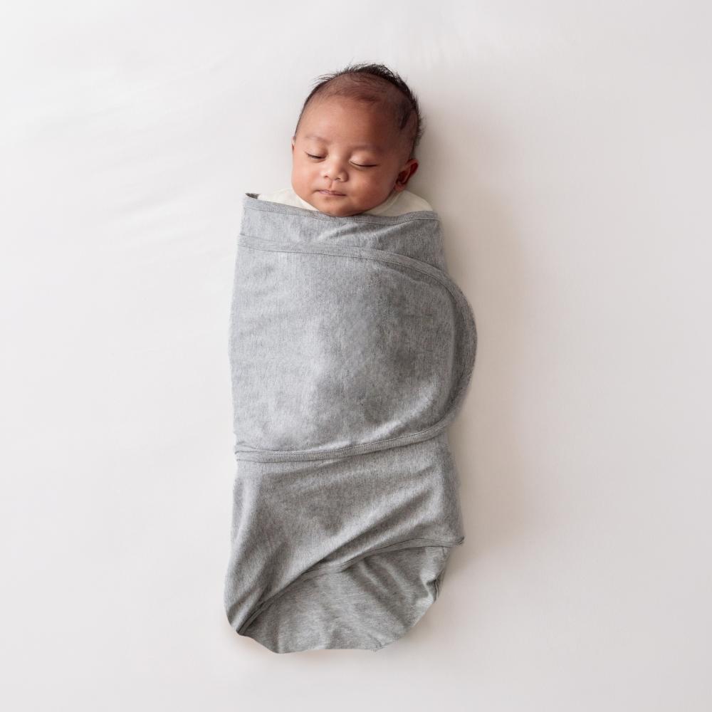 Newborn baby wrapped in a grey miracle blanket swaddle on a white background