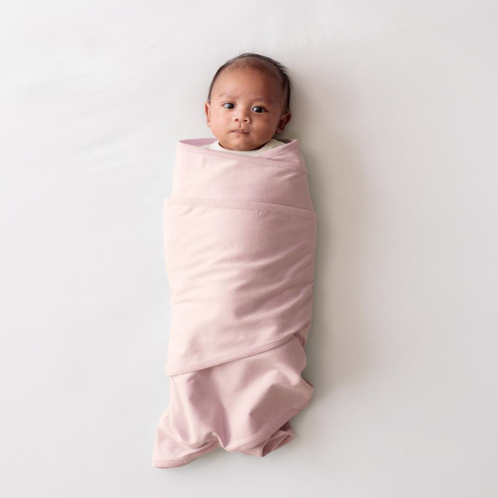 Newborn baby wrapped in a light pink miracle blanket swaddle on a white background