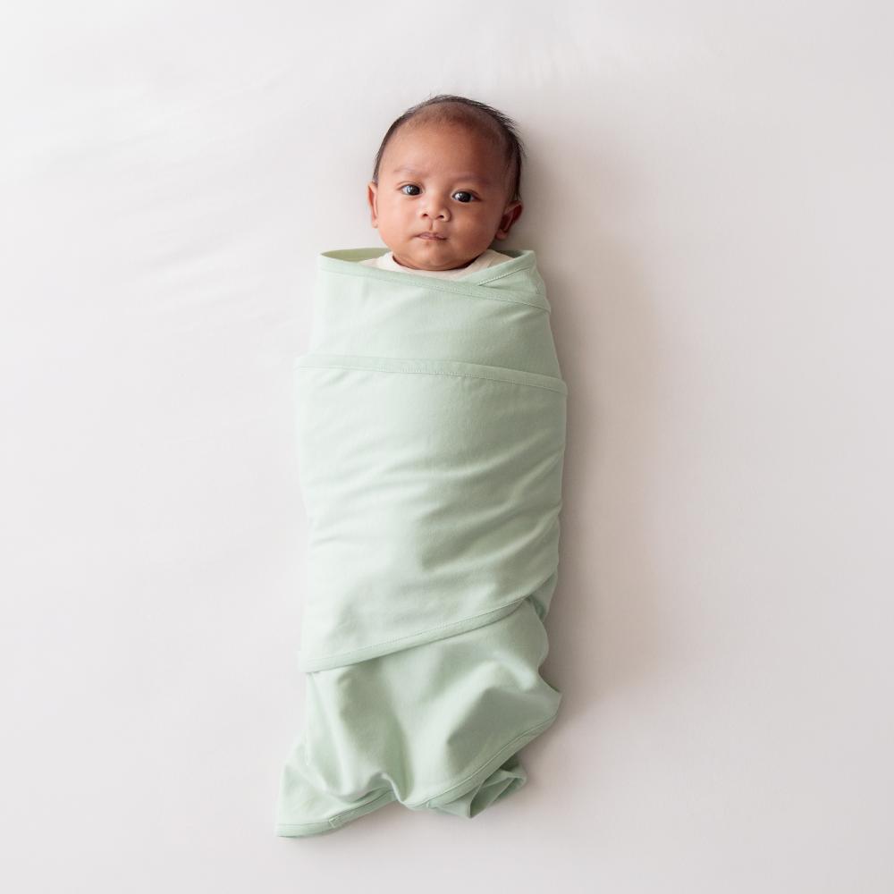 Baby wrapped in a light green miracle blanket swaddle on a white background