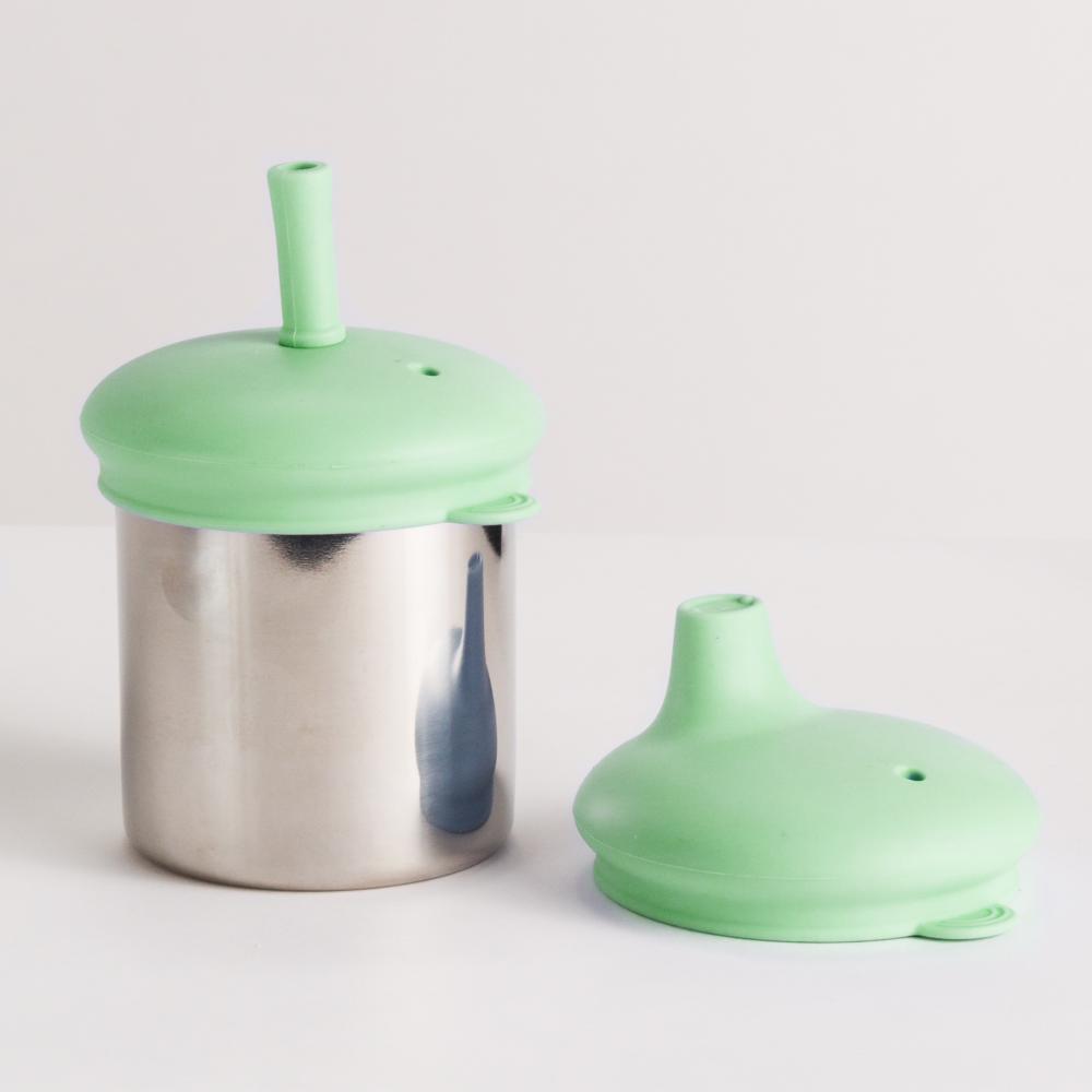 Green silicone lid on a stainless steel cup with another green sippy cup lid on a white background