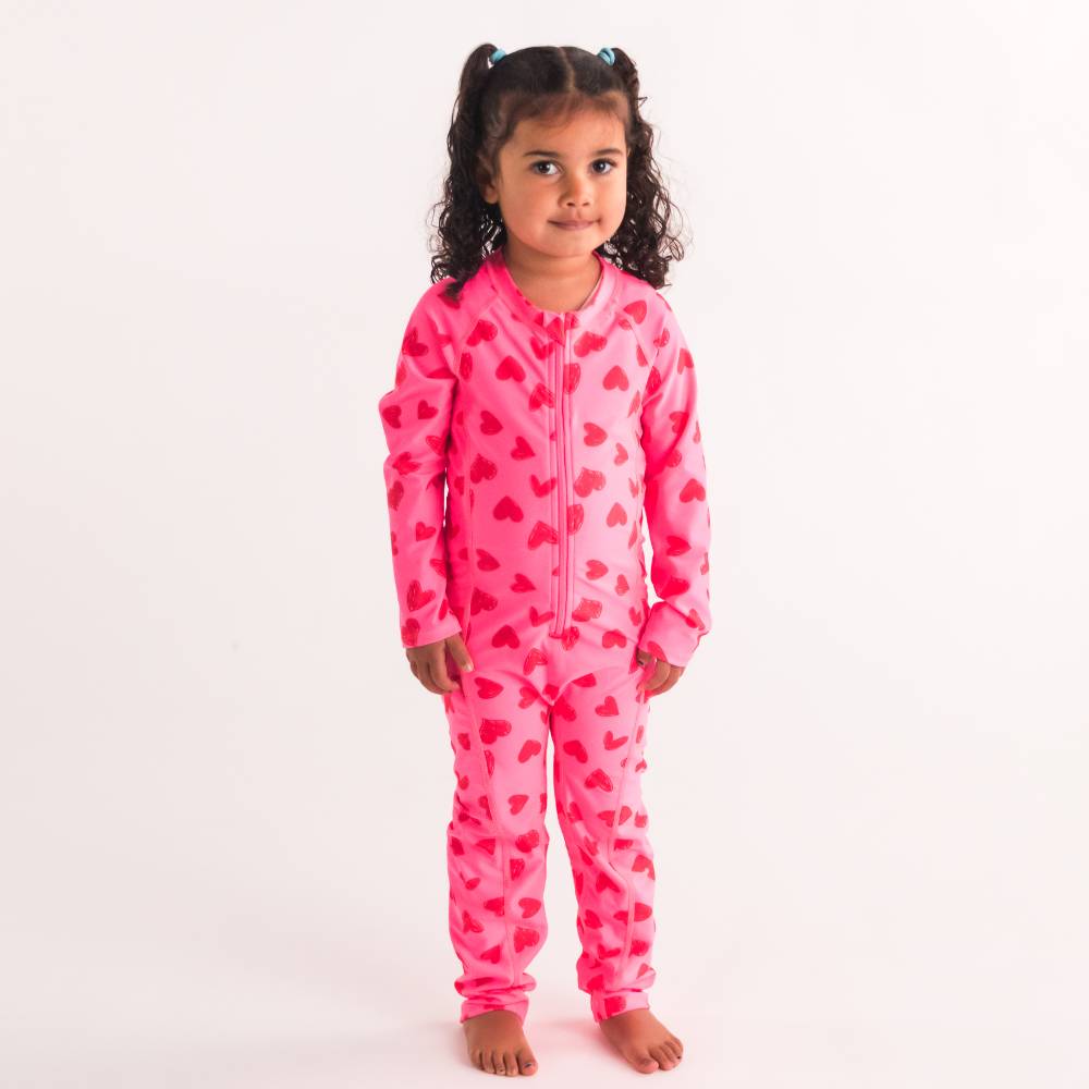 Child wearing a pink heart-patterned swim suit on a white background