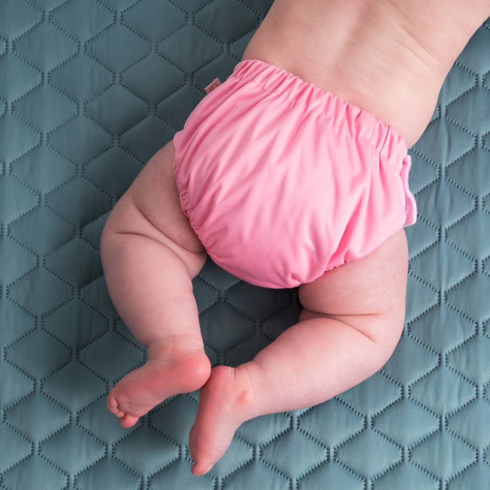 Baby wearing a reusable pink swim nappy on a textured blue surface