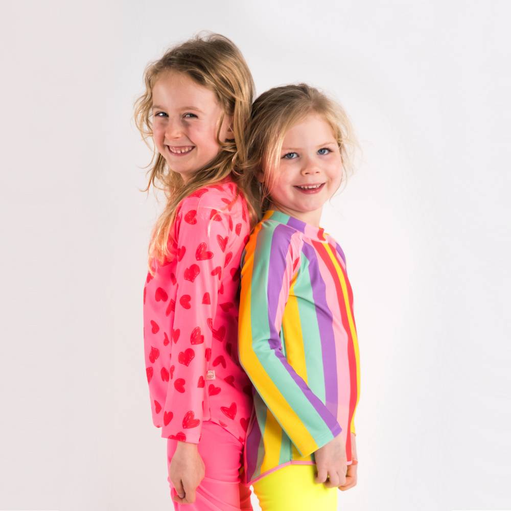 Two children wearing colorful swim rash vests with hearts and stripes on a white background