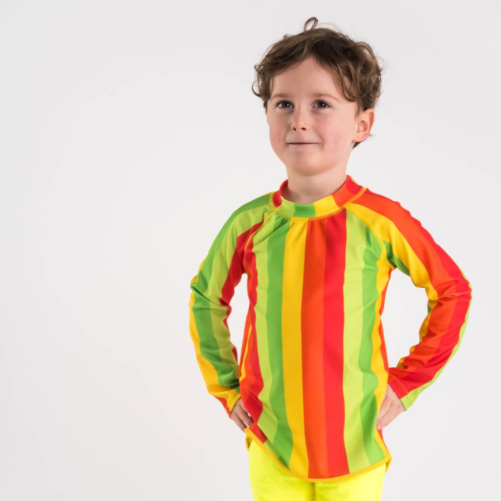 Child wearing a colorful striped swim rash vest and shorts on a white background