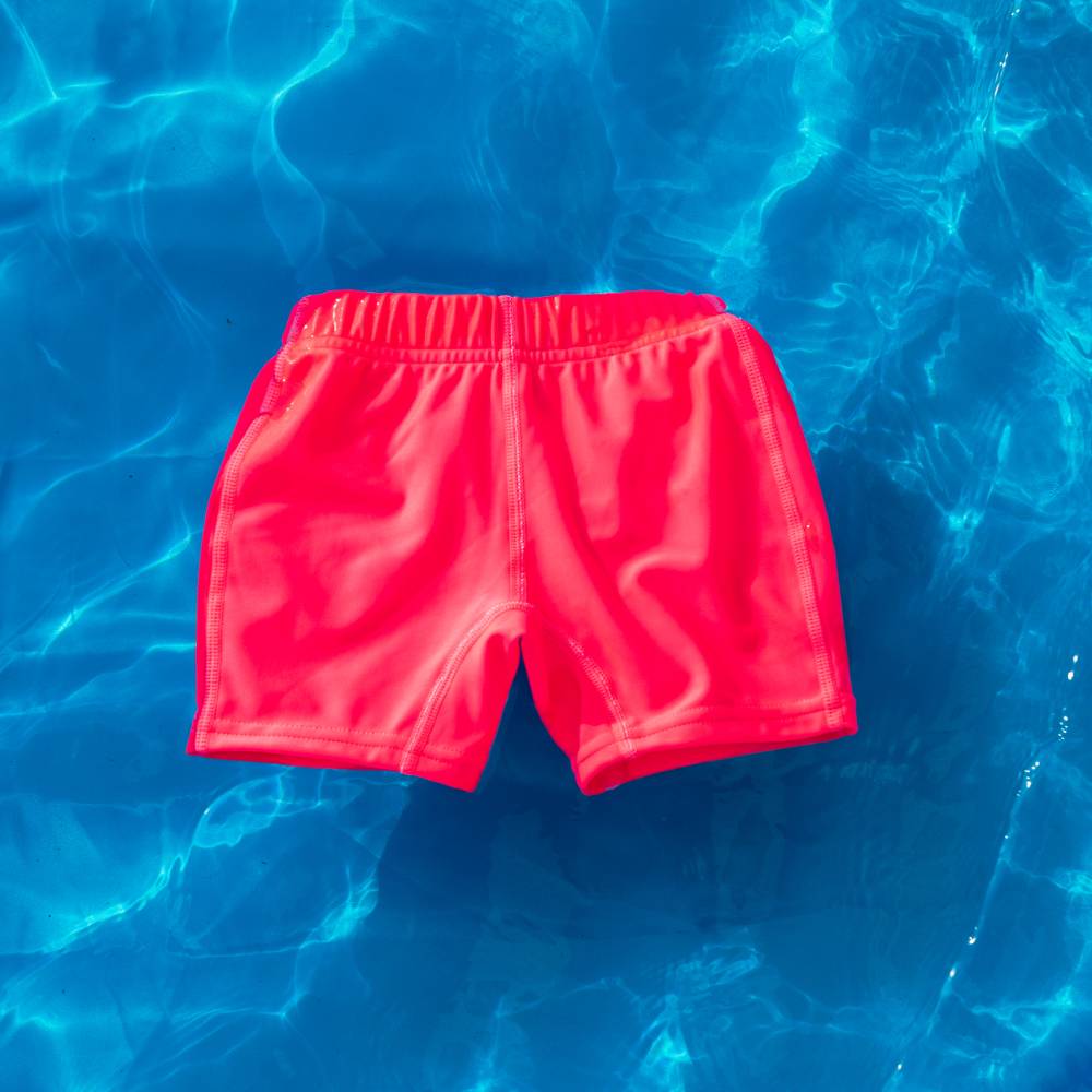 Bright neon pink swim jammers floating in clear blue water