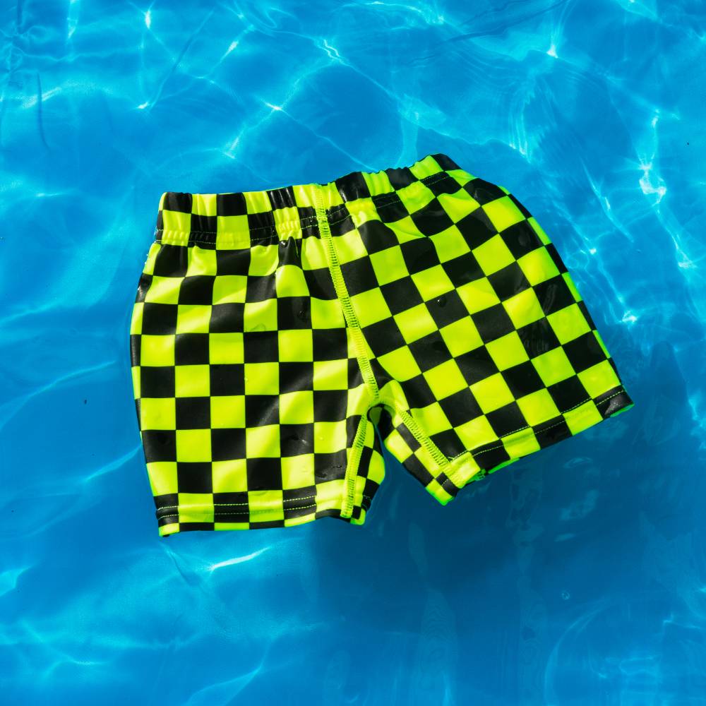 Checkered neon swim shorts on a blue water background