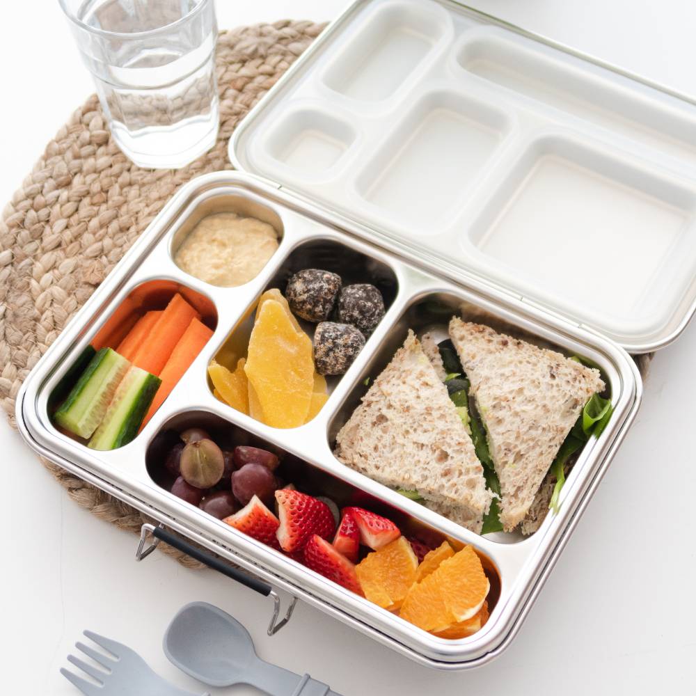 Bento box with a sandwich, fruits, and vegetables on a white surface.