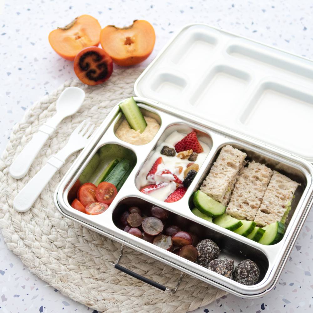 Divided lunch container with assorted food items on a textured surface