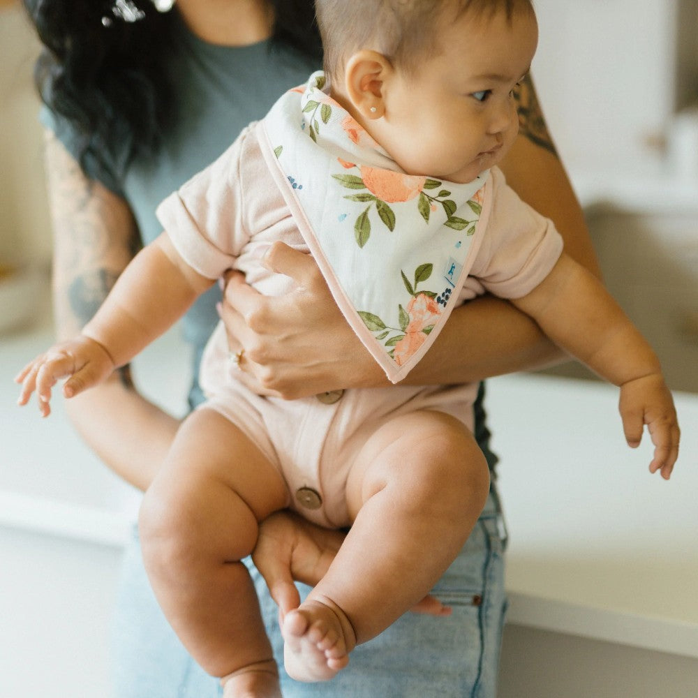 Baby wearing a floral bib being held by an adult indoors.